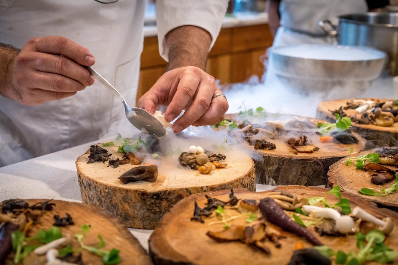 A chef artfully plating a gourmet dish with mushrooms and greens on wood slices.